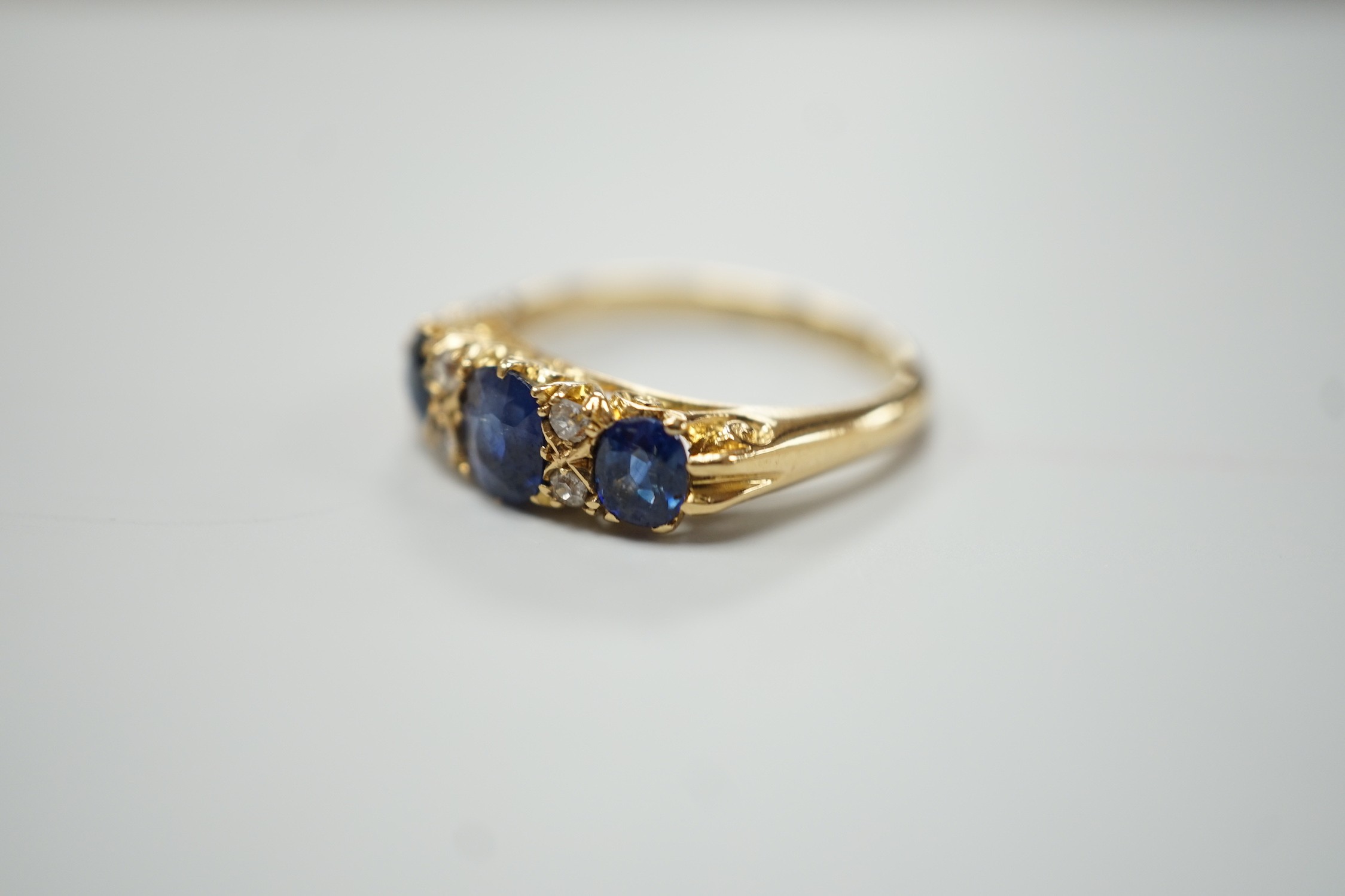 A George V 18ct gold and three stone sapphire set half hoop ring, with four diamond chip spacers, size M, gross weight 4.4 grams.
